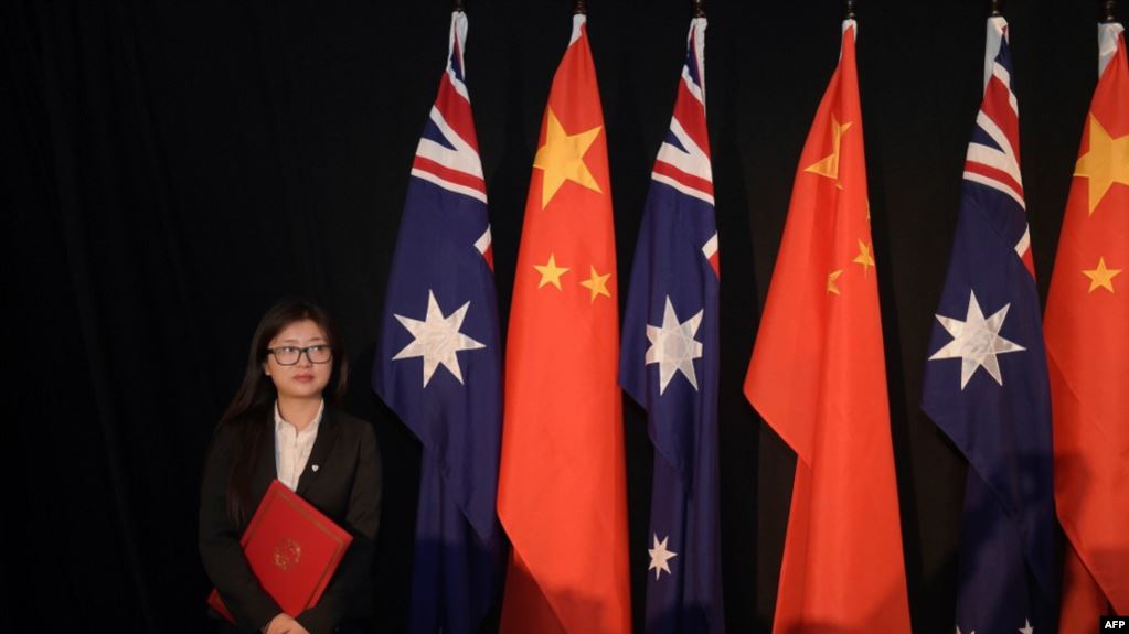 资料照：一名女子手持一本自由贸易协议站在中澳国旗旁。（2015年6月17日）