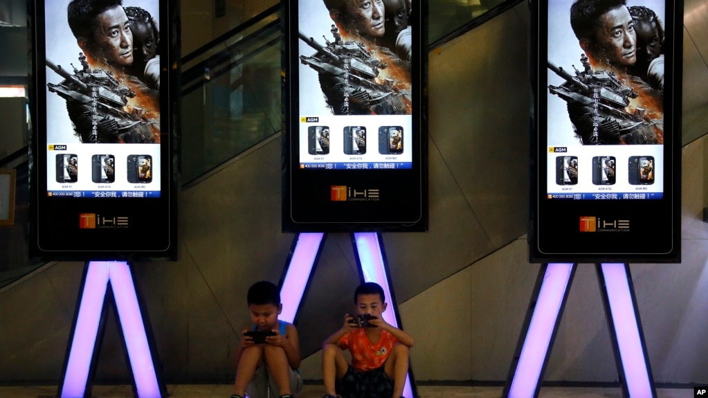 资料照：中国儿童在北京一家影院张贴的“战狼2”电影广告下玩手机。（2017年8月10日）