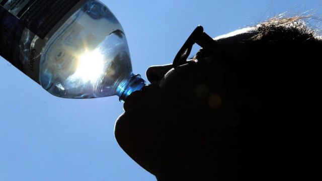A person drinking from a water bottle with sun shining through the bottle