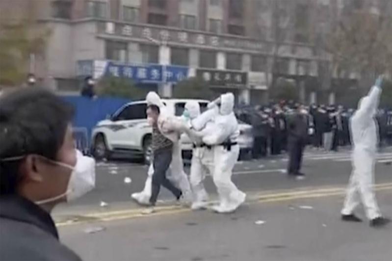 郑州富士康厂区昨天深夜爆发大规模新进劳工抗争。图为一名工人被身著白色防护衣的警察...