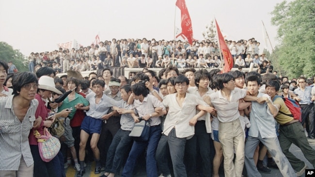 资料照片：1989年6月3日在北京人民大会堂附近，支持民主的抗议者手挽手阻止愤怒的人群追逐撤退的士兵。（美联社）
