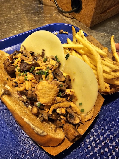 Caption: Mushroom Philly Sandwich is a flavorful blend of sauteed mushrooms, bell peppers, onions, and is topped with crispy spiced onions and Provolone cheese. It is served on a sourdough hoagie roll.
