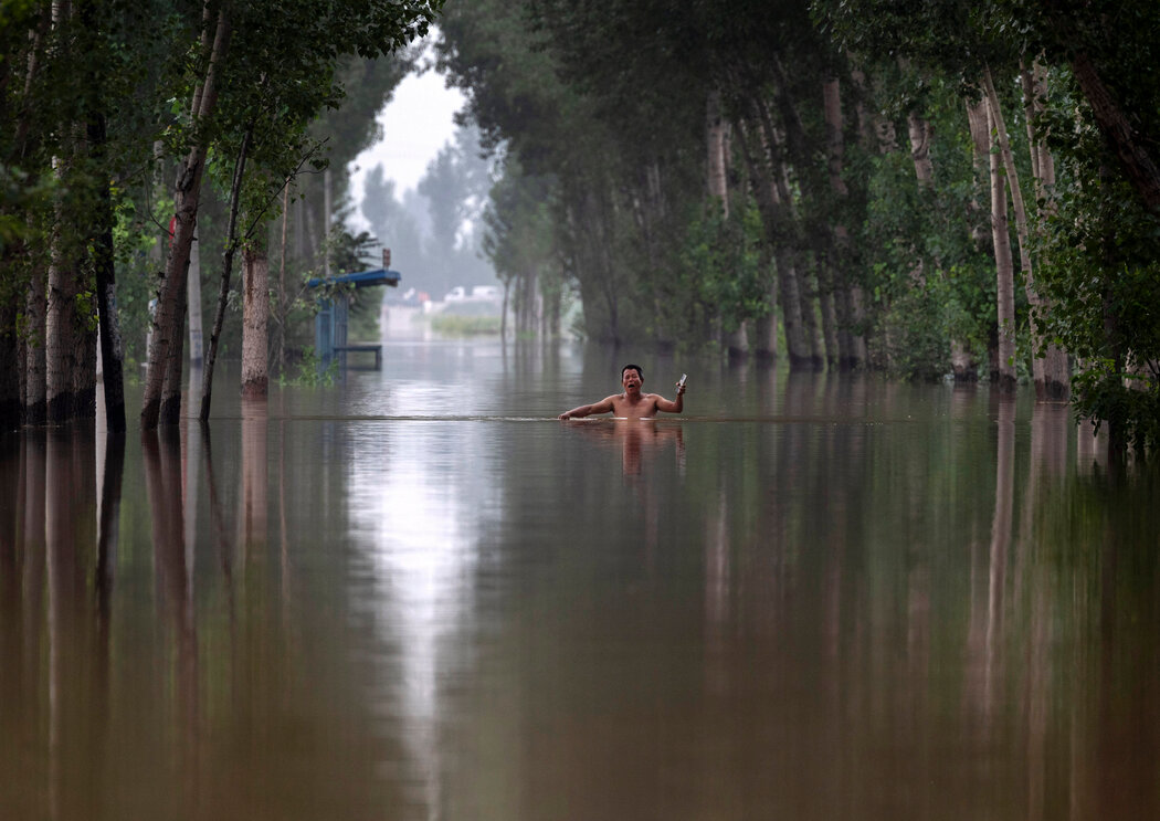 一位居民在涿州附近齐胸深的洪水中行走。