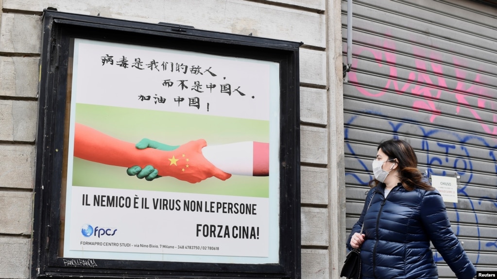 一名戴着口罩的妇女走过米兰街头一幅显示意大利与中国握手的广告牌。（2020年3月10日）(路透社)
