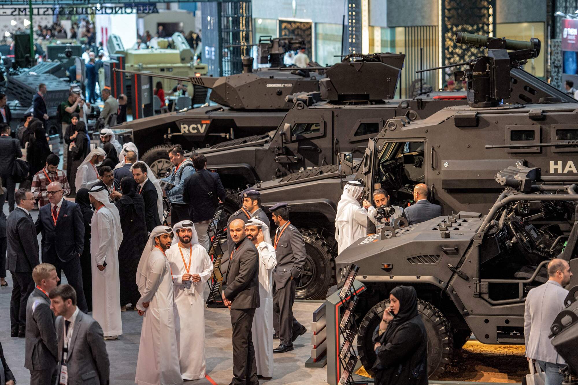 Visitors, some in suits and some in white robes with headdresses, check out brown-colored armored vehicles at weapons fair